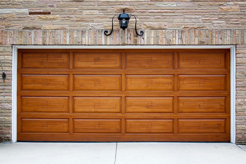 Brown wooden garage door with decorative panels, on a brick wall, under a black lantern.
