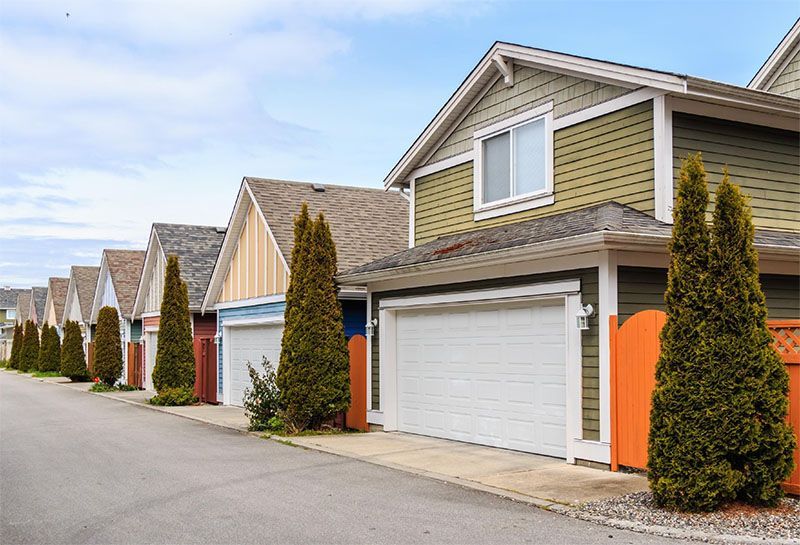 Row of colorful townhouses with garages, green trees line the street, blue sky.