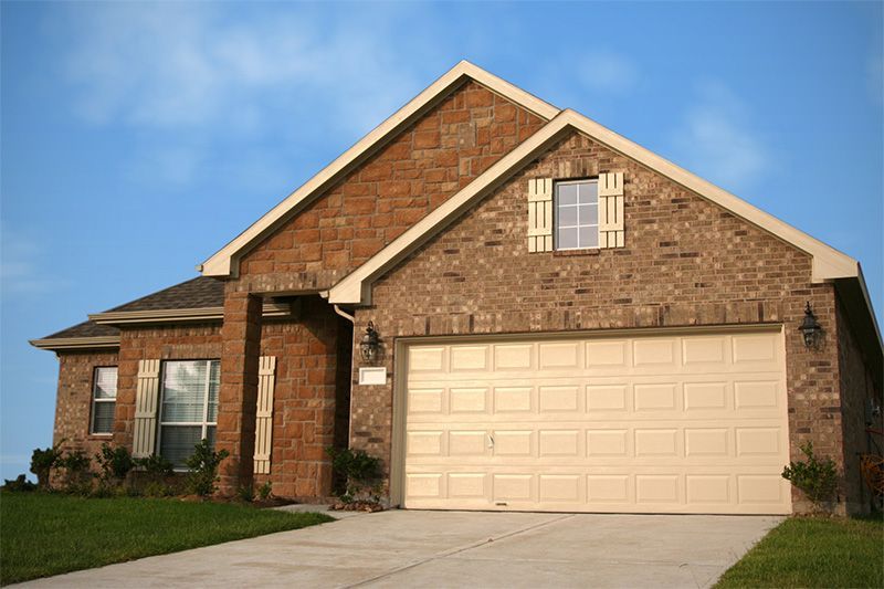 Brick house with beige garage door, cream shutters, and blue sky.