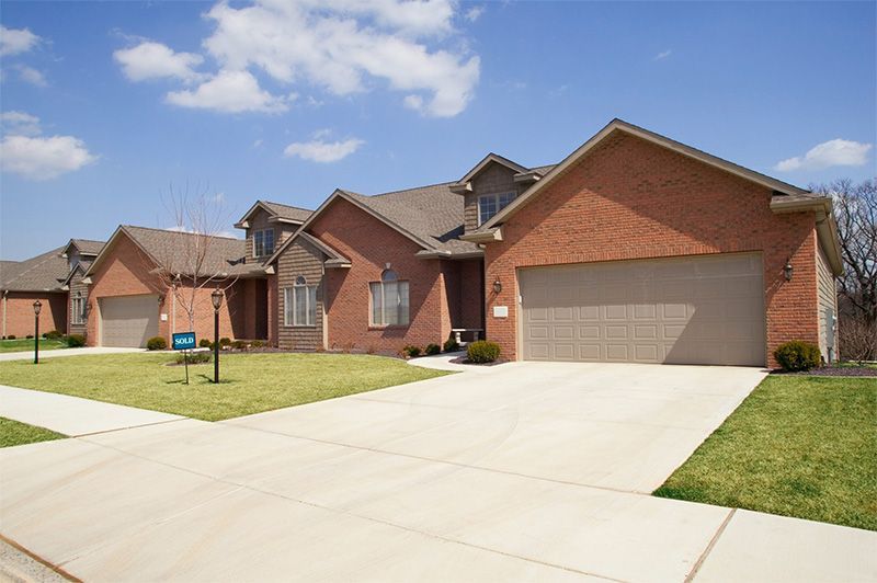 Row of brick houses with attached garages and driveways, on a sunny day.