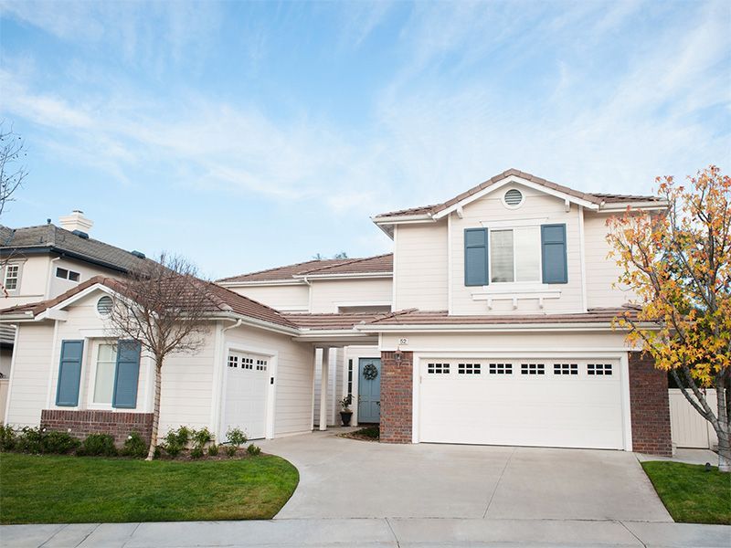 Two-story white house with a garage, blue shutters, and a driveway on a sunny day.