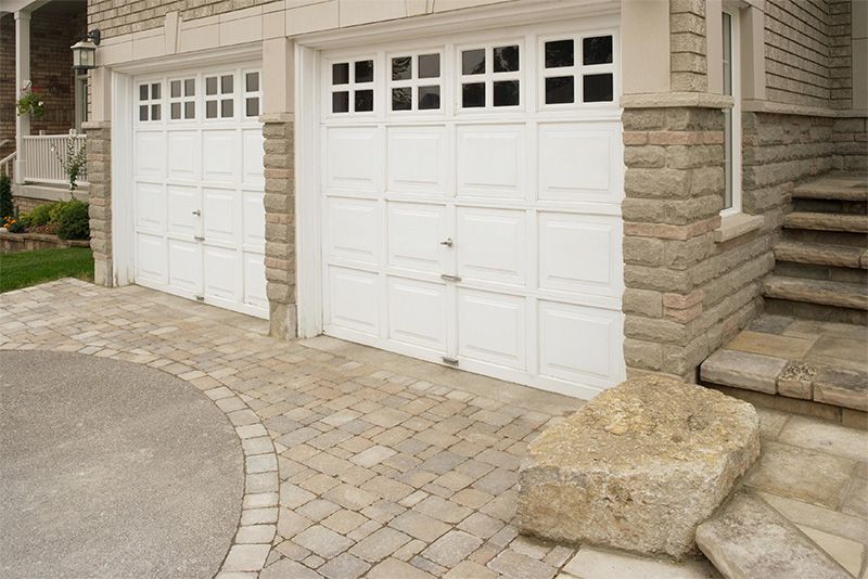 Two white garage doors with glass panels; stone facade and paved driveway.