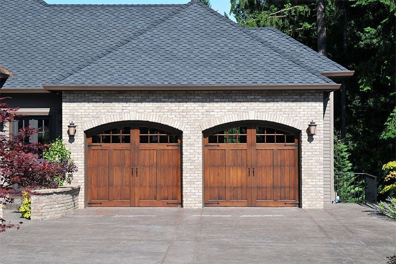 Two brown wooden garage doors under brick facade and dark roof.