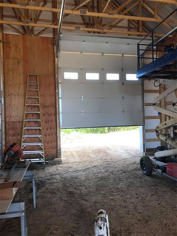 Interior of a partially constructed building with a partially open garage door. A ladder, tools, and lift are present.