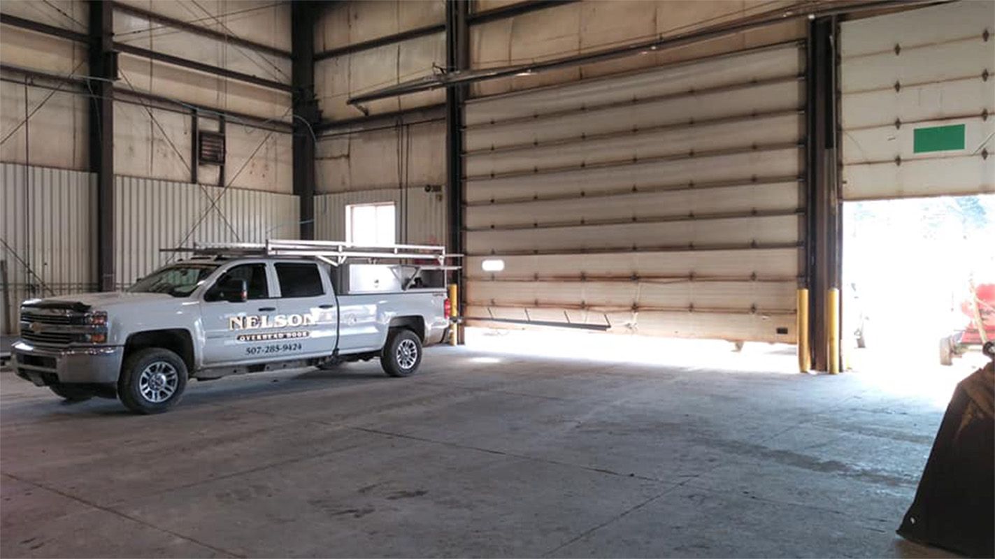 A silver truck parked inside a warehouse with an open garage door; sunlight streams in.