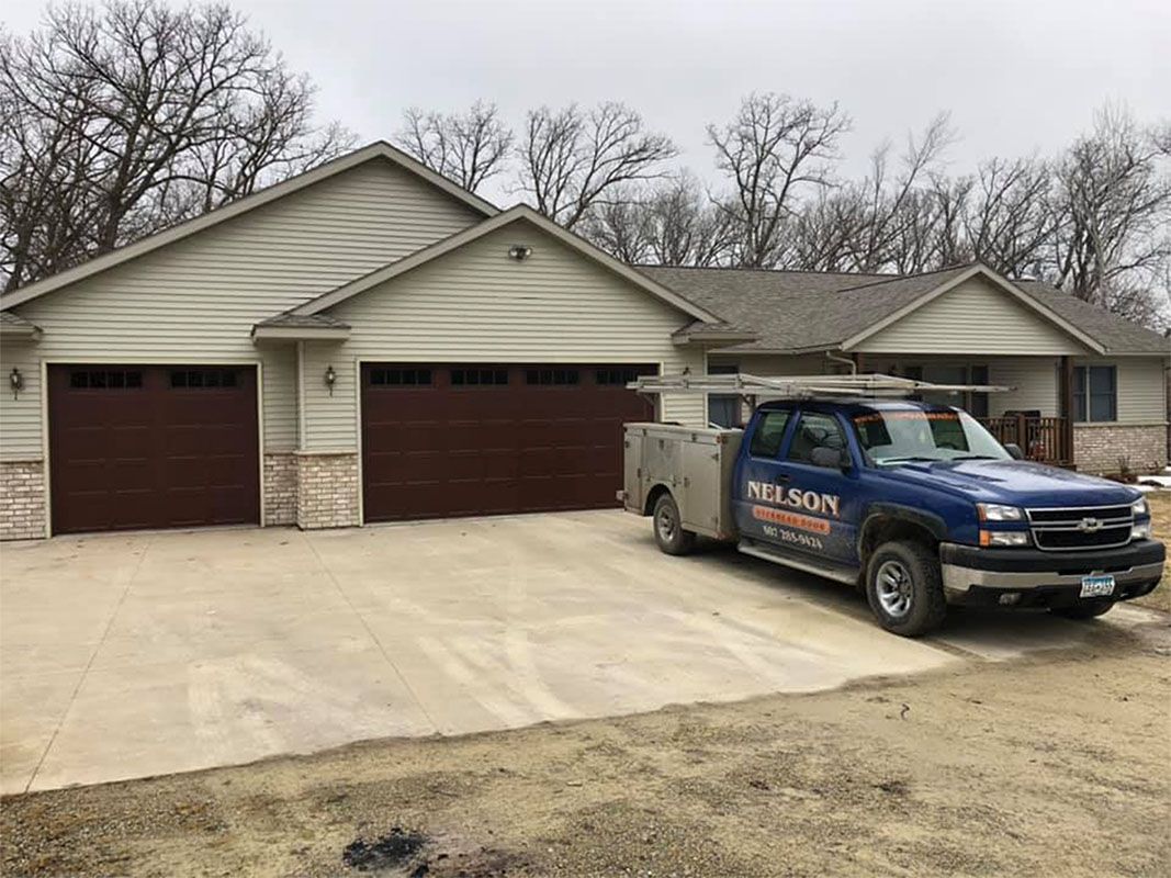 Blue work truck parked in front of a house with brown garage doors.