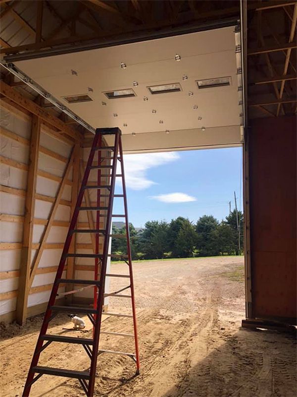 Red ladder inside a building with a large open doorway, white overhead door, and a bright outdoor view.
