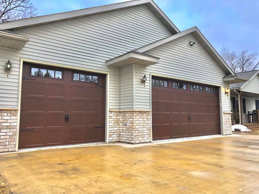 Brown garage doors with windows on a light-colored building with stone accents.