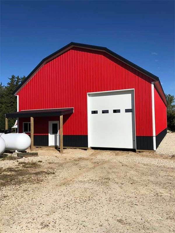 Red barn with black trim, a large white garage door, and small covered entrance; sunny outdoors.