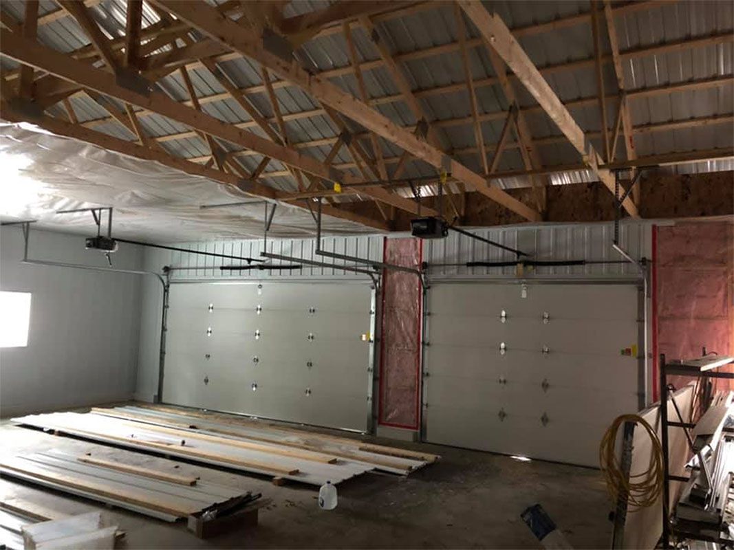 Interior of a garage with two closed white doors, exposed wooden beams, and insulation.
