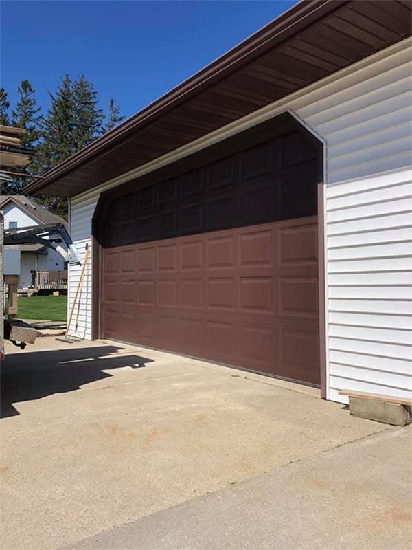 Brown garage door on a house with white siding and concrete driveway.
