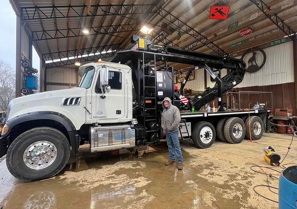 A man is standing in front of a large truck in a garage.