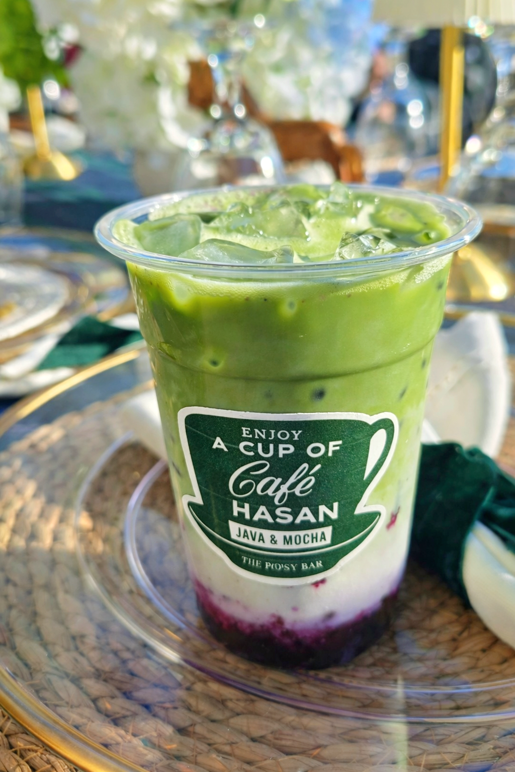 A clear plastic cup of iced matcha layered with a dark purple fruit base, featuring a 