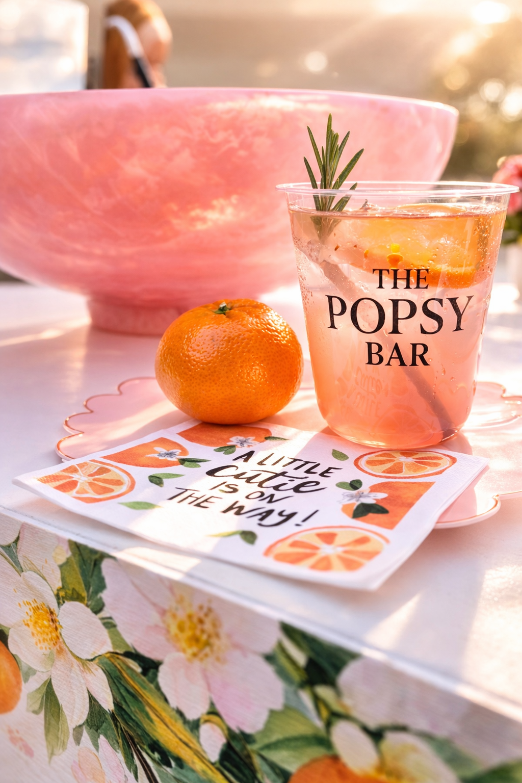 A drink at a baby shower with a pink bowl, a mandarin orange, and a napkin reading, 