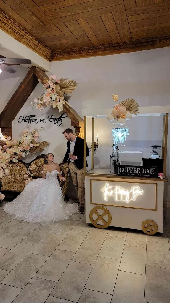 Bride and groom by a popcorn cart. Bride in white dress sits, groom stands, both near floral decor.