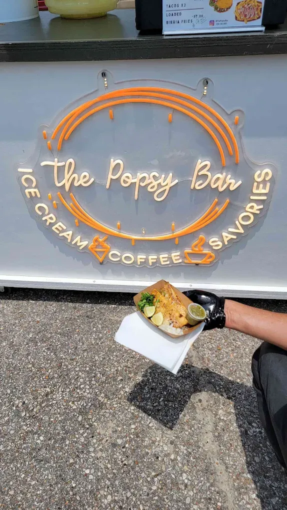 Person holding a savory dish in front of a food stand with a neon sign: 