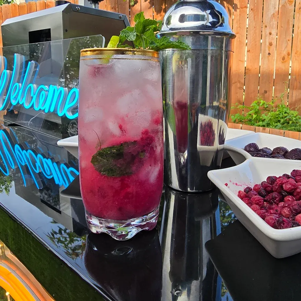 Cocktail with raspberries, mint, ice, and lime on a black bar with shaker and berries.