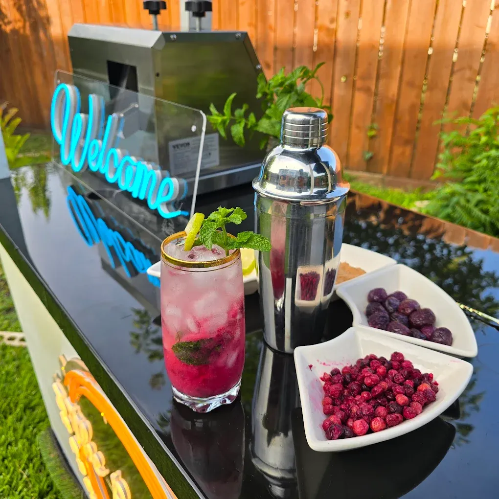 Outdoor cocktail bar with a drink, shaker, garnishes, and a 