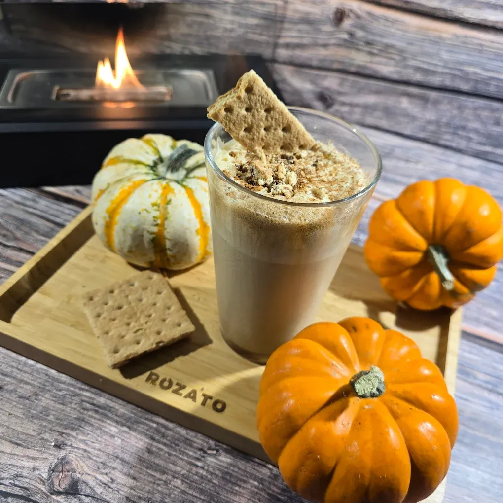 Pumpkin spice drink with graham cracker, pumpkins, and a fire in a cozy setting.