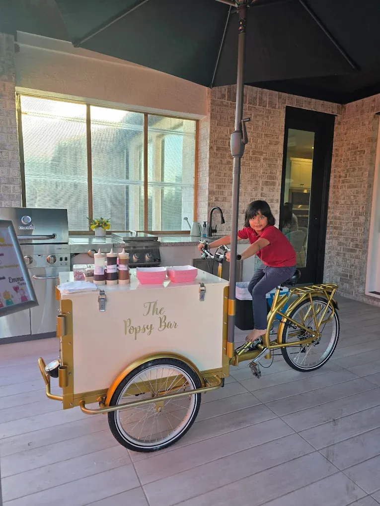 A child sits on a gold and white ice cream trike labeled 