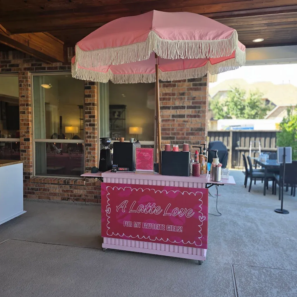 Pink coffee cart under a fringe umbrella, in an outdoor setting.
