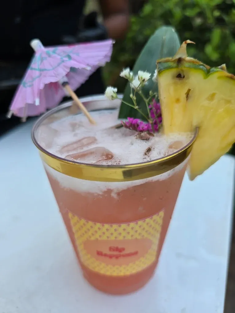 Cocktail in a gold-rimmed glass, garnished with pineapple, a paper umbrella, and flowers.