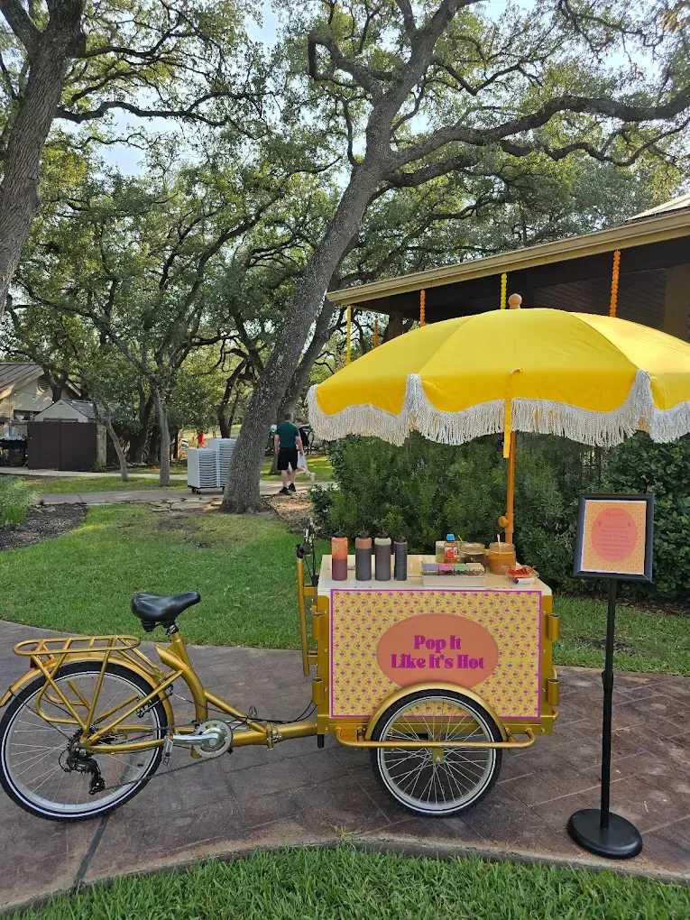 Yellow ice pop cart on a bicycle under a yellow umbrella in a park, 