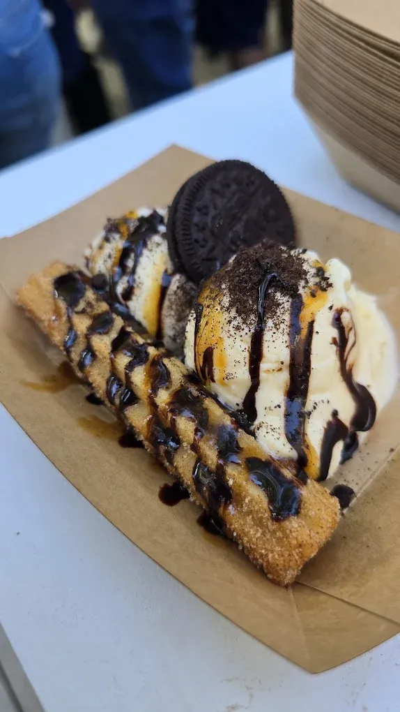Fried churro dessert with ice cream, chocolate sauce, and an Oreo cookie on a cardboard tray.