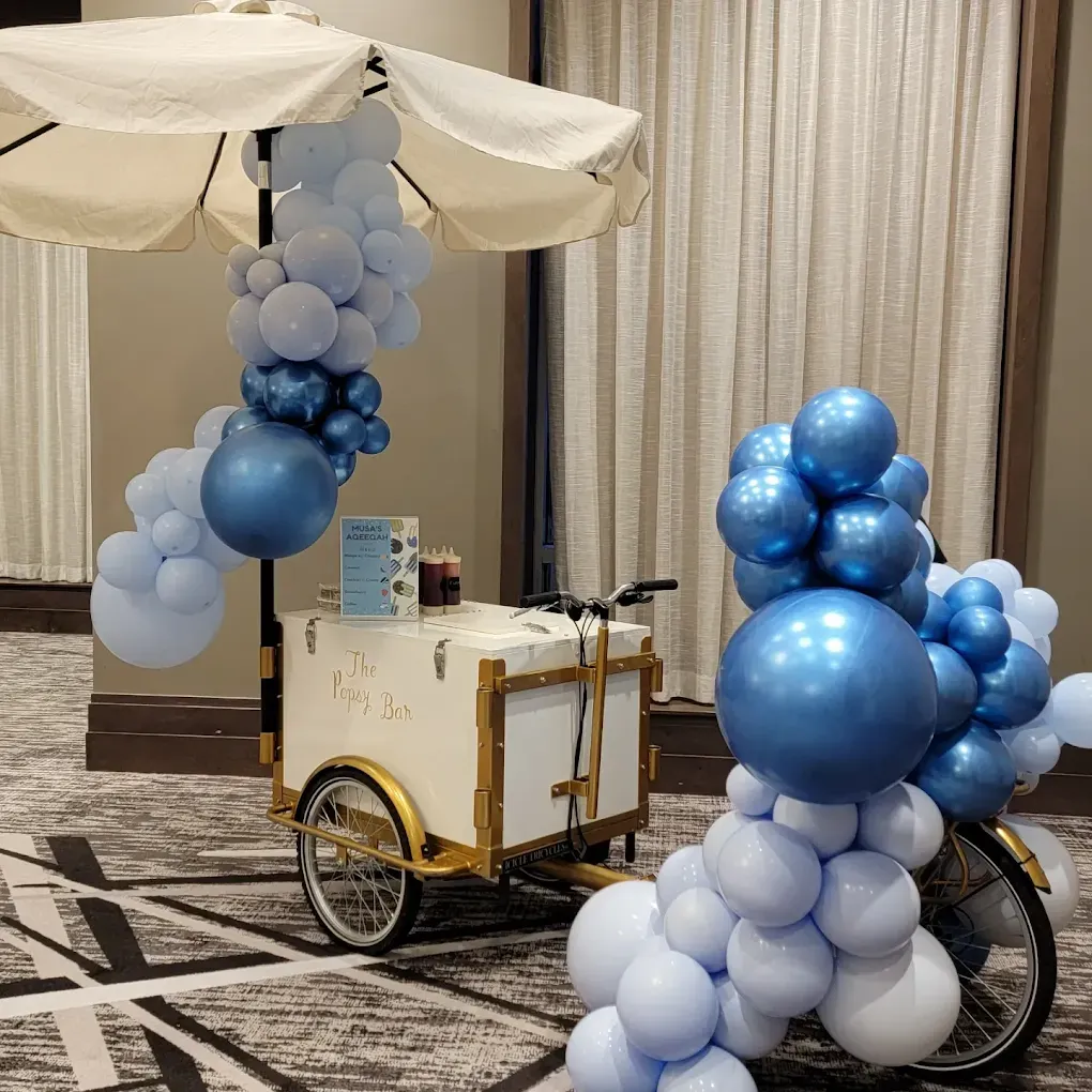 Ice cream cart decorated with blue balloons and a white umbrella.
