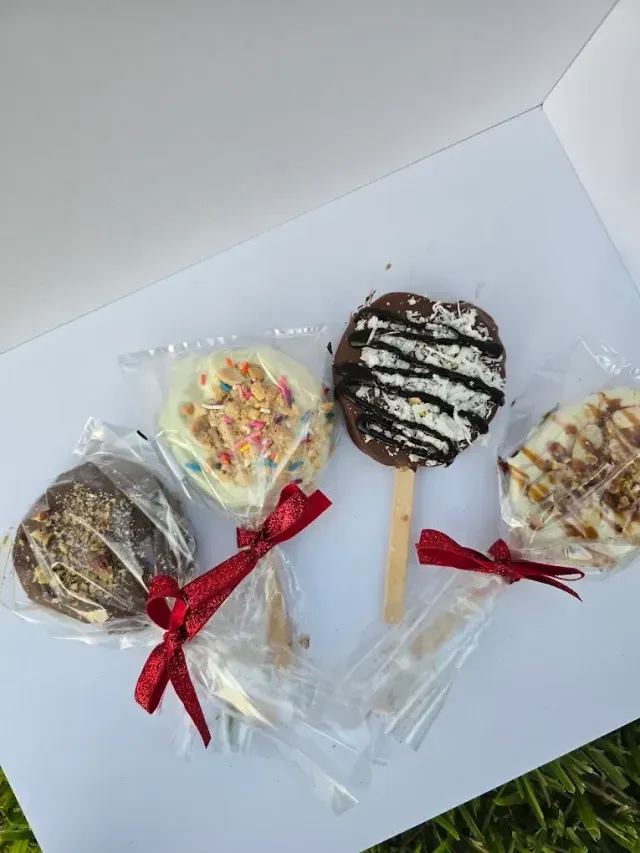 Four decorated chocolate-covered apple pops, individually wrapped in clear plastic with red ribbon bows.