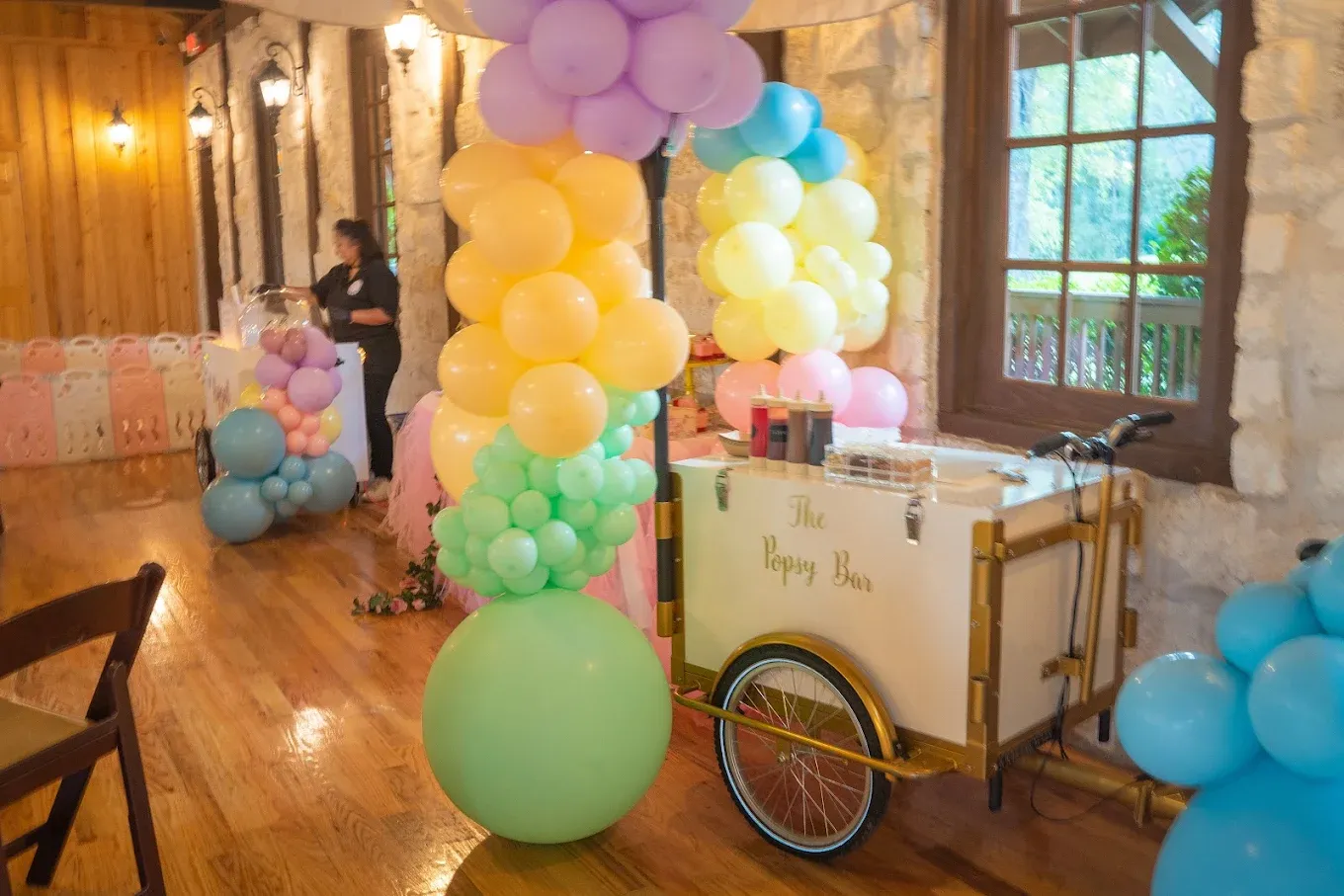 Party scene with balloon arch, cart, and decorations; indoors.