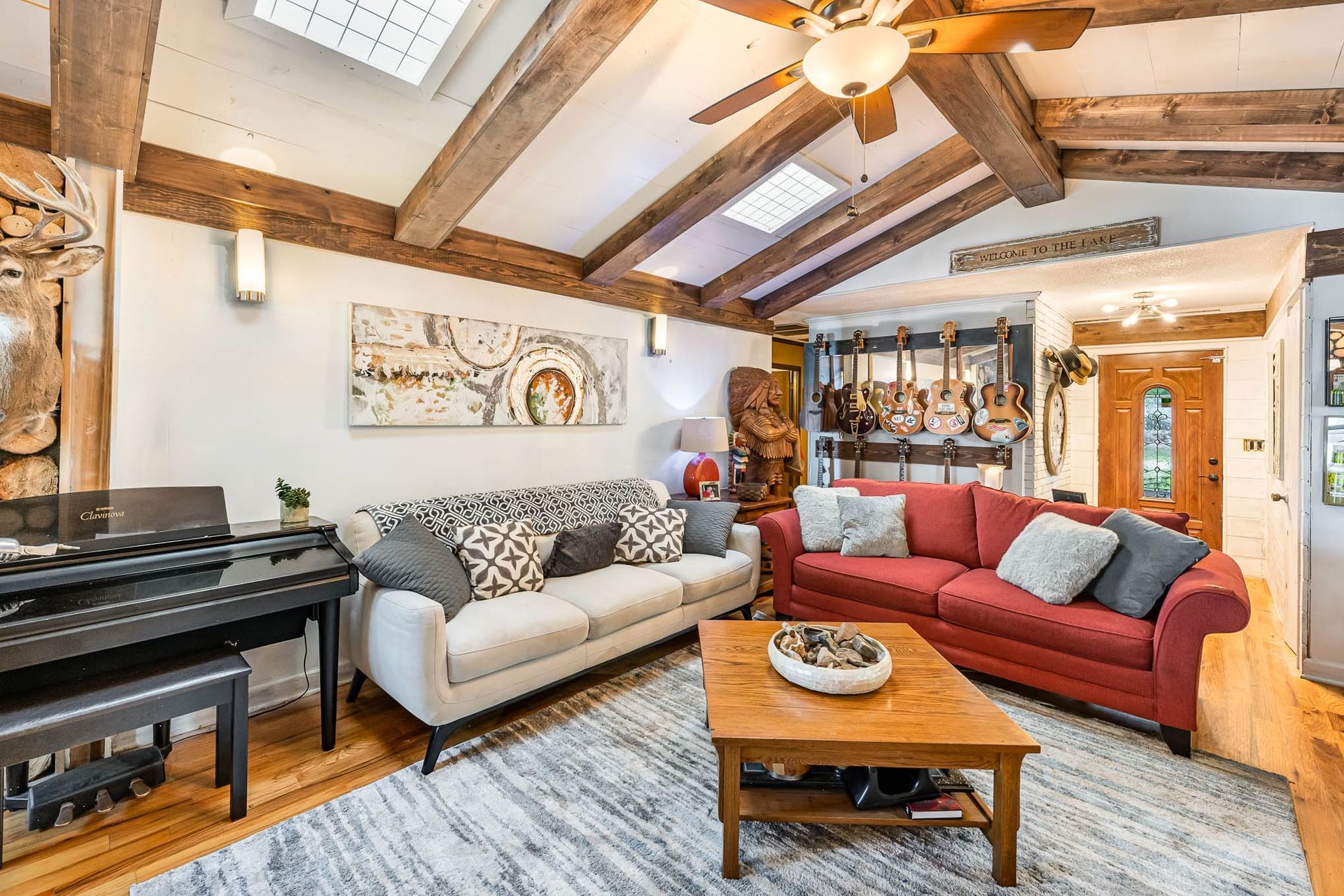 Cozy living room with piano, red and beige sofas, wooden coffee table, exposed beams, and warm lighting