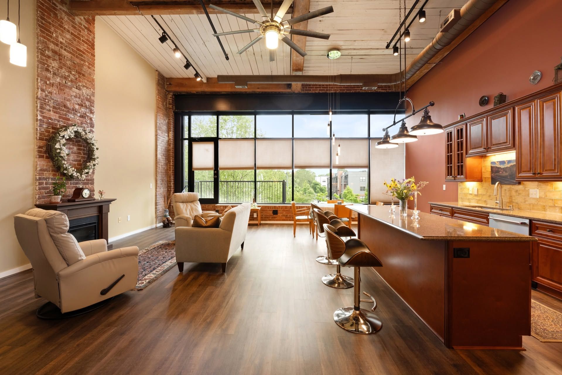 Modern open-plan living room and kitchen with leather chairs, wood floors, and large windows