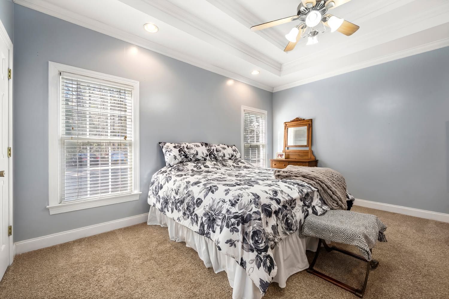 Bright bedroom with gray walls, carpet, floral bedspread, dresser, and ceiling fan.
