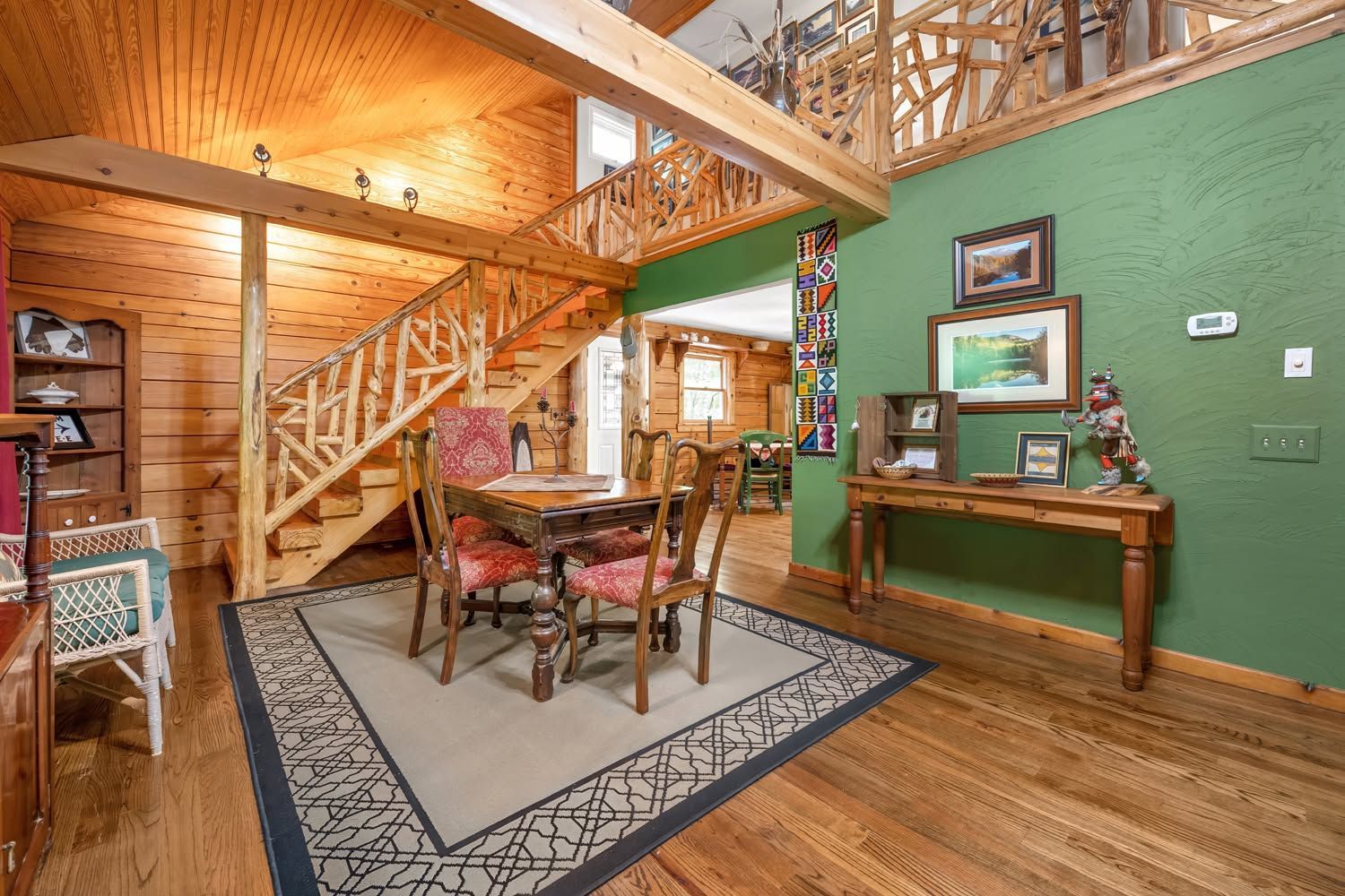 Rustic cabin living room with wooden staircase, green wall, and dining table over a patterned rug