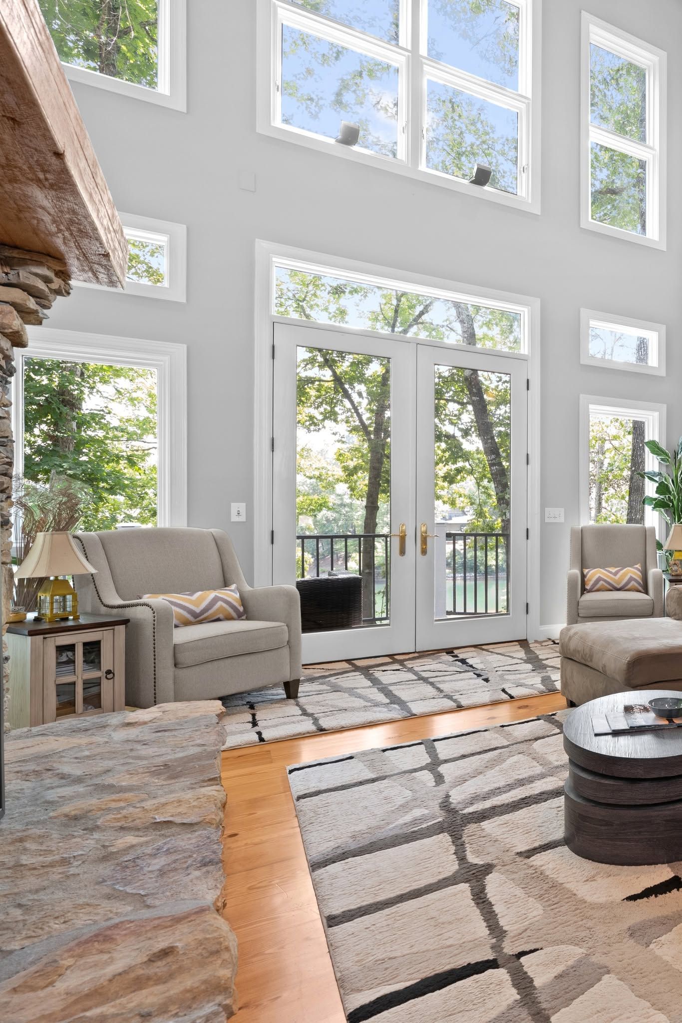 Bright, airy living room with tall windows, a glass door, neutral sofas, and patterned rugs on a wooden floor