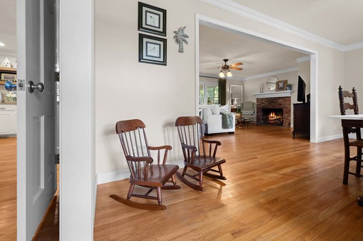 Living room with hardwood floors, two wooden chairs, and a view into a kitchen and fireplace area