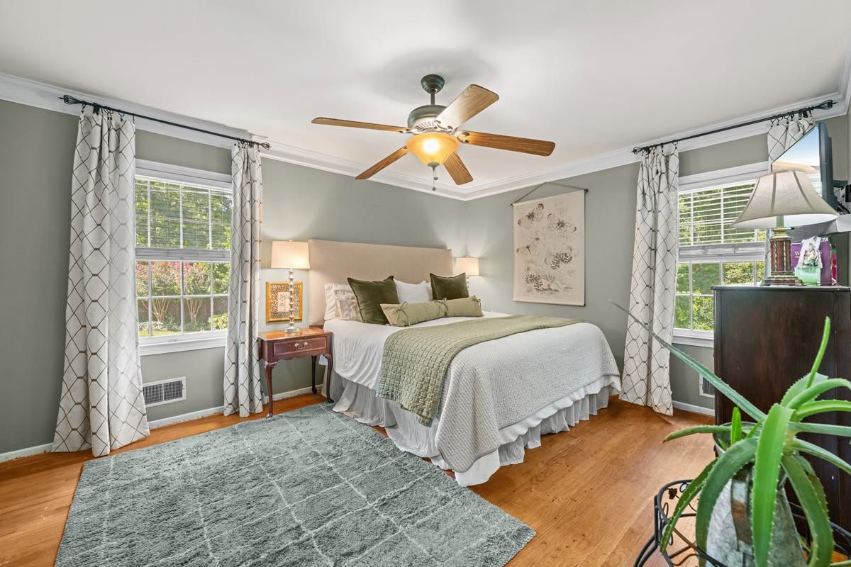 Bright bedroom with a bed, ceiling fan, large windows, wood floors, and gray rug