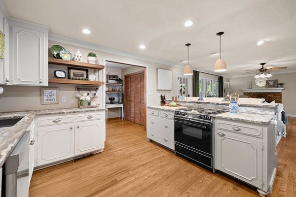 Bright white kitchen with wood floors, black stove, island, and open shelving under recessed lights