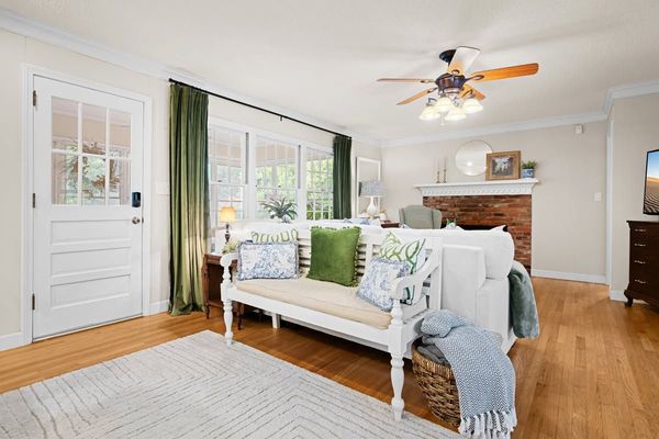 Bright living room with white sofa, green curtains, wood floors, fireplace, and ceiling fan