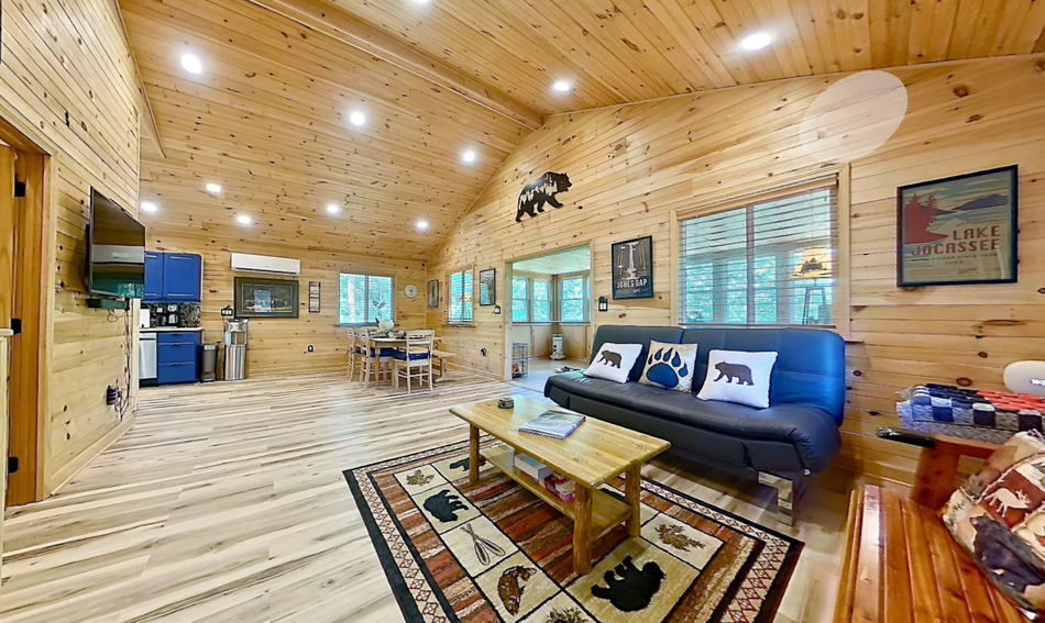 Cozy wood-paneled living room with sofa, coffee table, rug, and large windows; Zillow 3D tour overlay