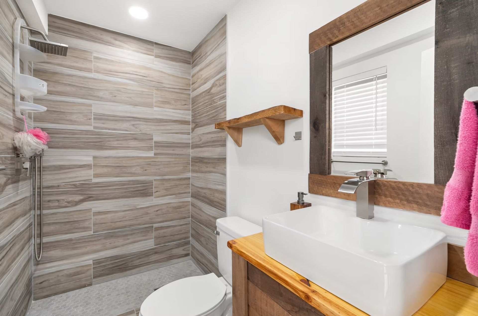 Modern bathroom with tiled shower, white sink, mirror, and wooden accents