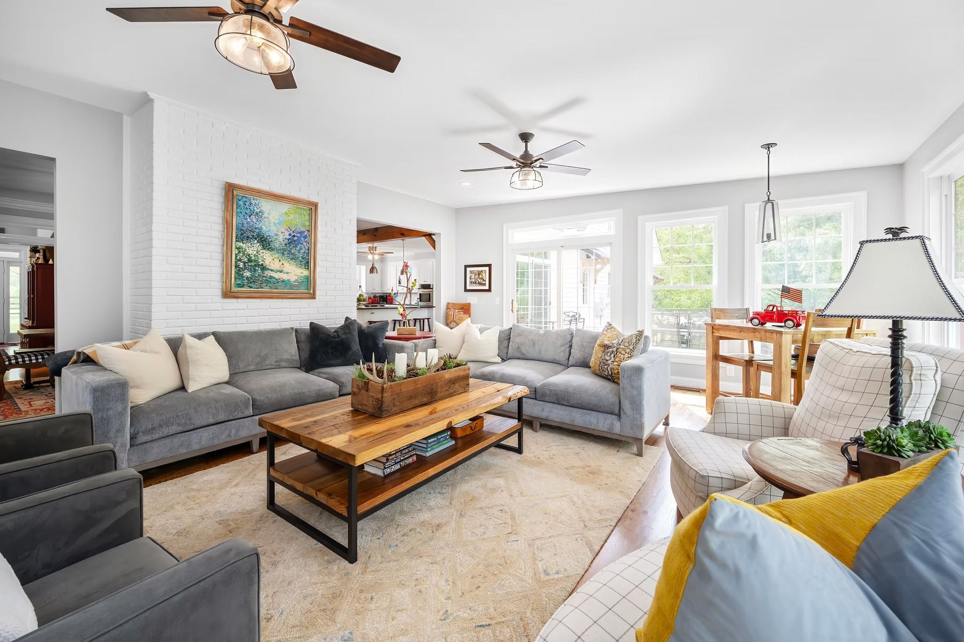 Bright living room with gray sofas, colorful pillows, coffee table, and ceiling fans near large windows