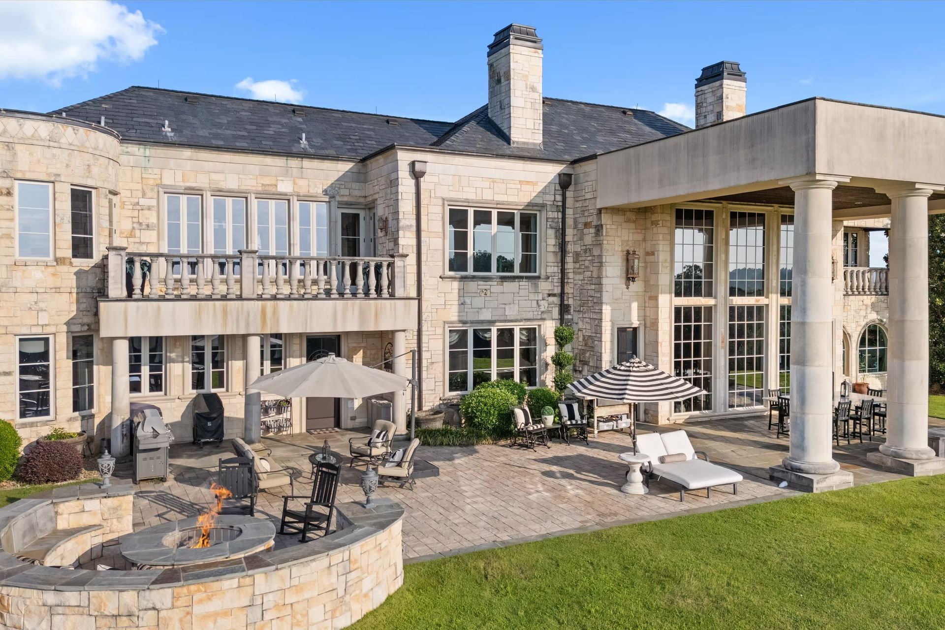 Stone manor house with patio, outdoor seating, and columns overlooking a green lawn