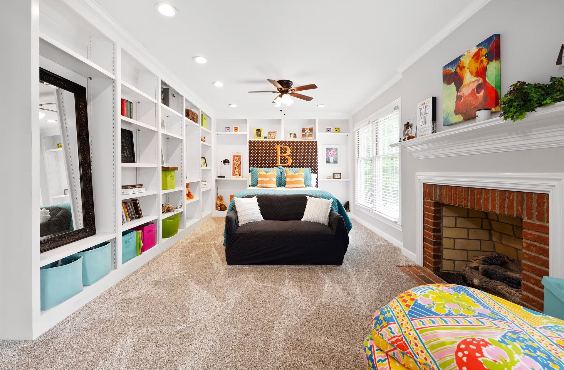 Bright living room with white built-ins, black sofa, fireplace, and colorful decor
