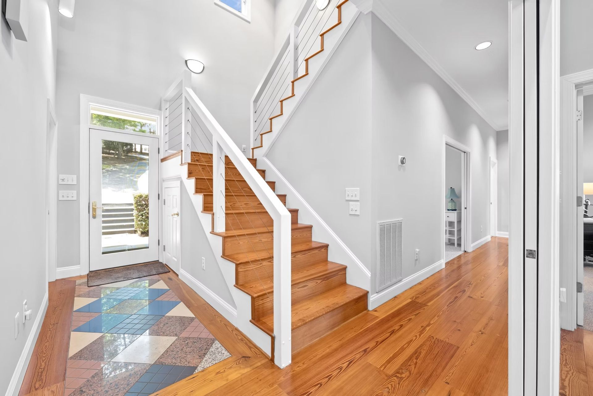 Bright foyer with white staircase, colorful tile entry, and warm wood floors