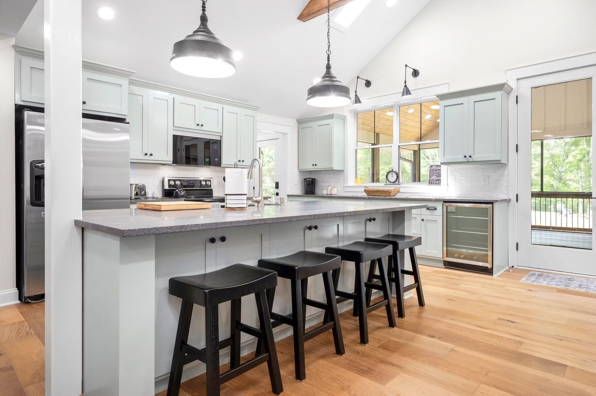 Bright modern kitchen with white cabinets, island seating, pendant lights, and hardwood floors