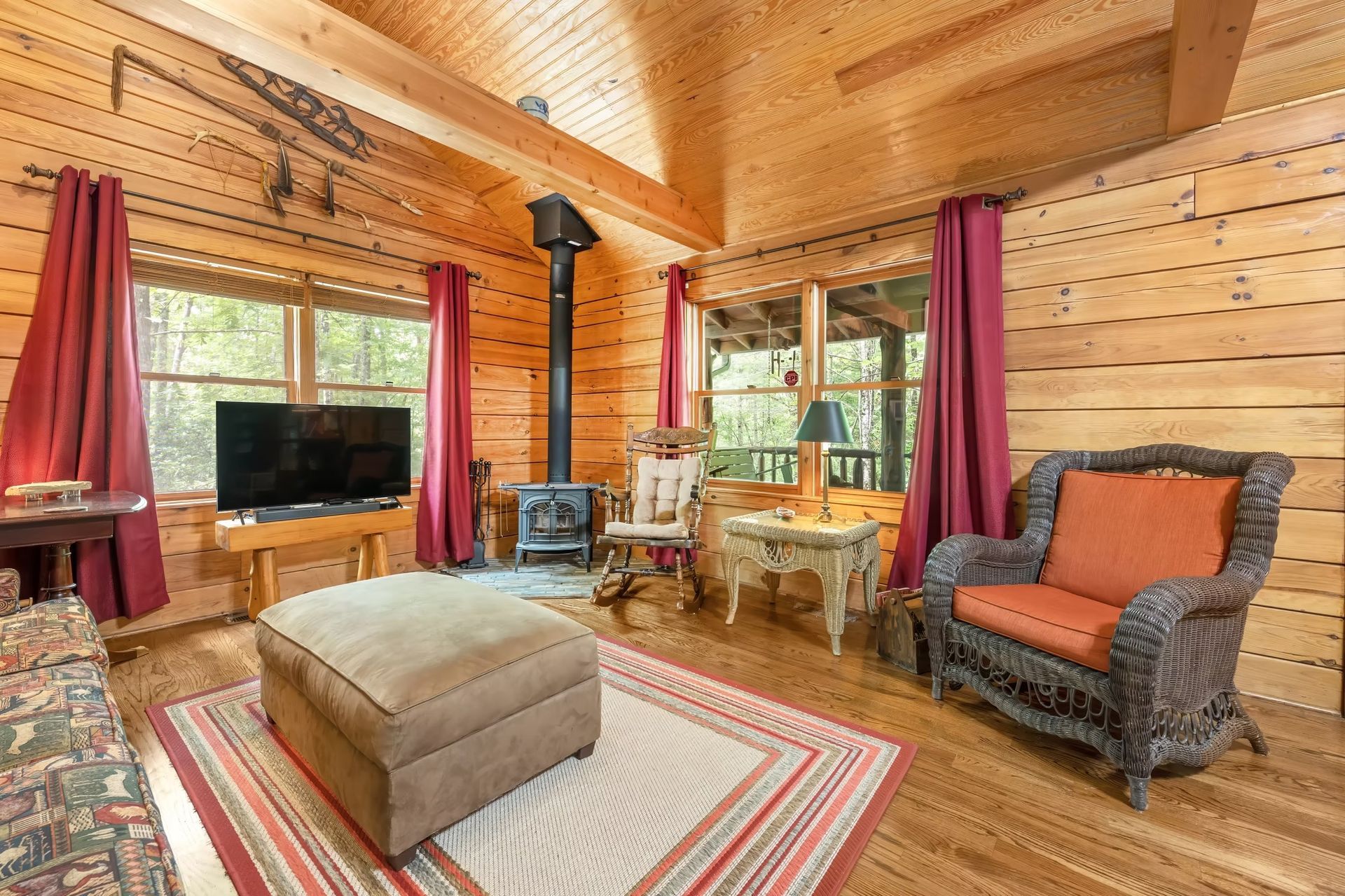 Cozy log cabin living room with wood walls, red curtains, fireplace, TV, and patterned sofa.