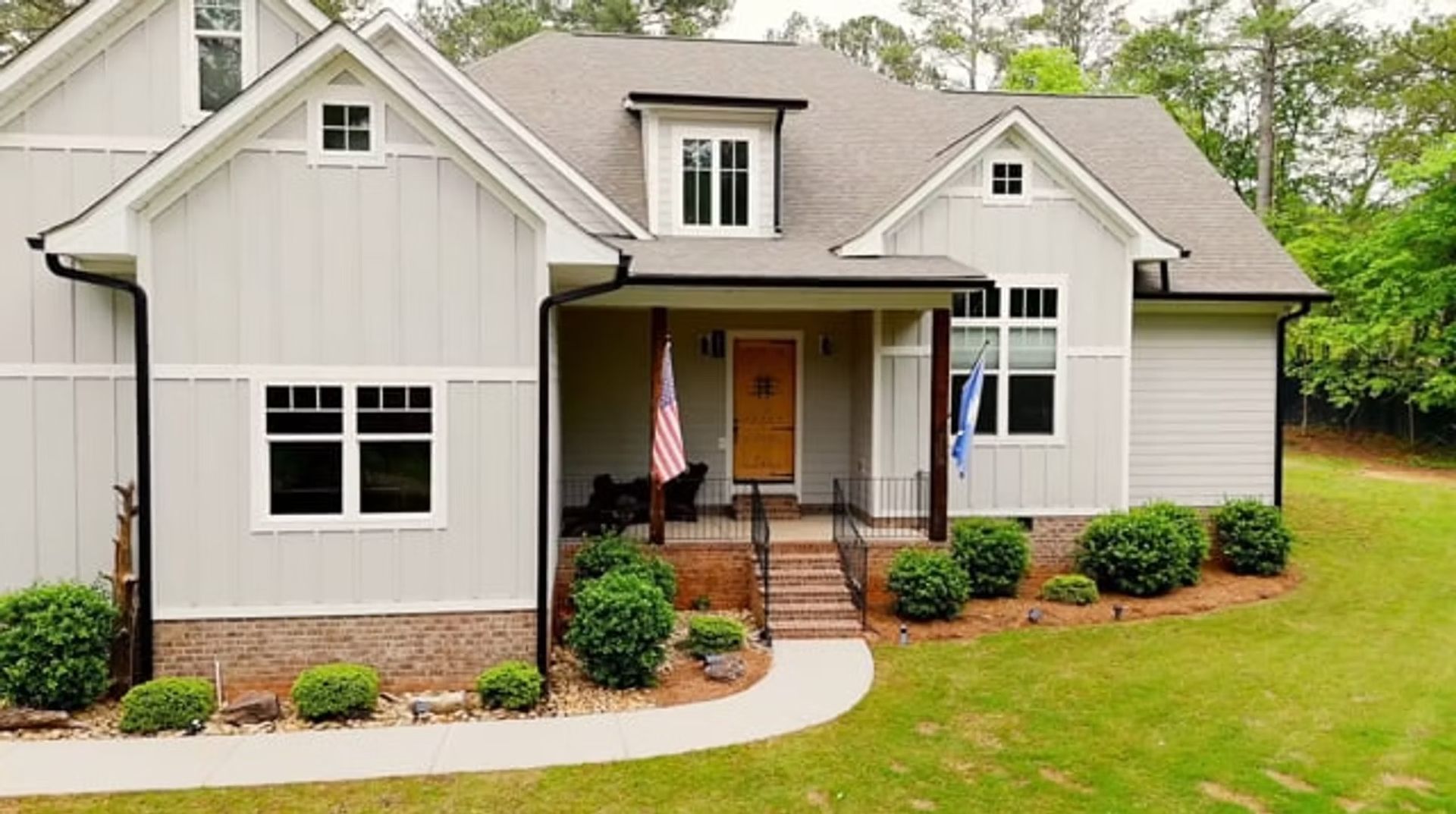 Single-story gray house with white trim, front porch, and a curved walkway in a landscaped yard.