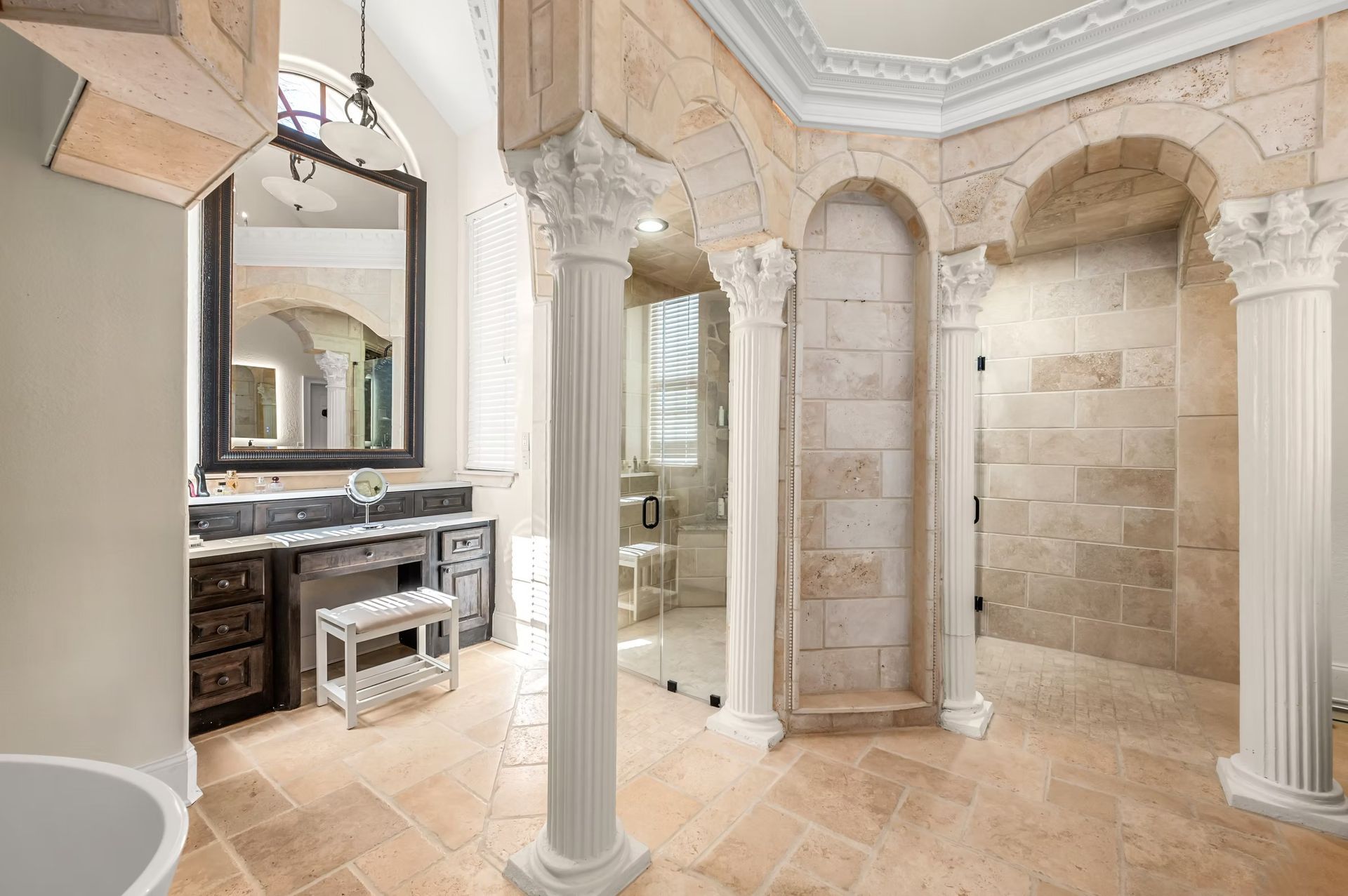 Elegant marble bathroom with arched columns, ornate ceiling, vanity, and tiled shower area